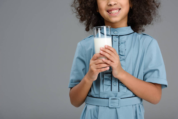 abgeschnittene Aufnahme eines lächelnden kleinen Kindes mit einem Glas Milch isoliert auf grau - Foto, Bild