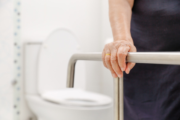 Starsza kobieta trzyma na poręcze w łazience. - Zdjęcie, obraz