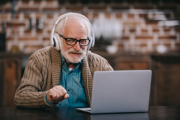 Homme âgé dans les écouteurs à l'aide d'un ordinateur portable
 - Photo, image