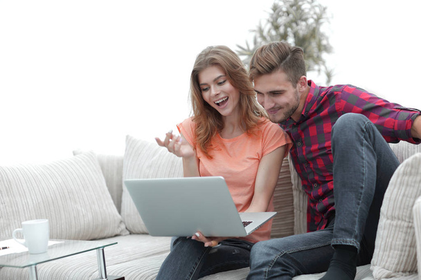 young man with his girlfriend looking at the laptop sitting on the sofa. - 写真・画像