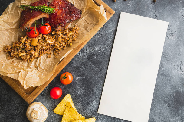 carne asada servida con tomates cherry y trigo sarraceno sobre papel artesanal con papel en blanco sobre fondo de piedra
 - Foto, Imagen