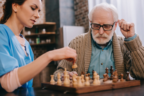 Enfermera y hombre mayor jugando ajedrez
 - Foto, Imagen