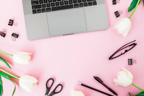 Draufsicht auf Laptop, umgeben von frischen Tulpen und Papeterie auf rosa Hintergrund - Foto, Bild