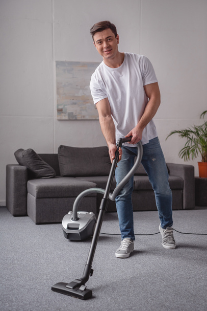 handsome man cleaning living room with vacuum cleaner - Fotó, kép