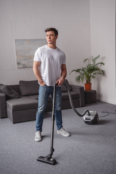 handsome man posing with vacuum cleaner in living room - Foto, imagen