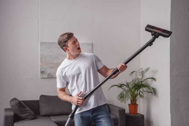 handsome man having fun with vacuum cleaner in living room - Photo, Image