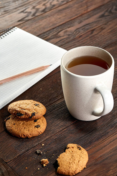 Чашка чая с печеньем, рабочая тетрадь и карандаш на деревянном фоне, вид сверху
 - Фото, изображение