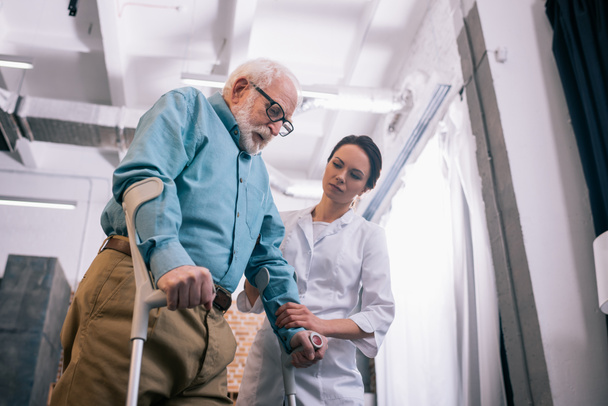 Arzt stützt männlichen Patienten mit Krücken - Foto, Bild