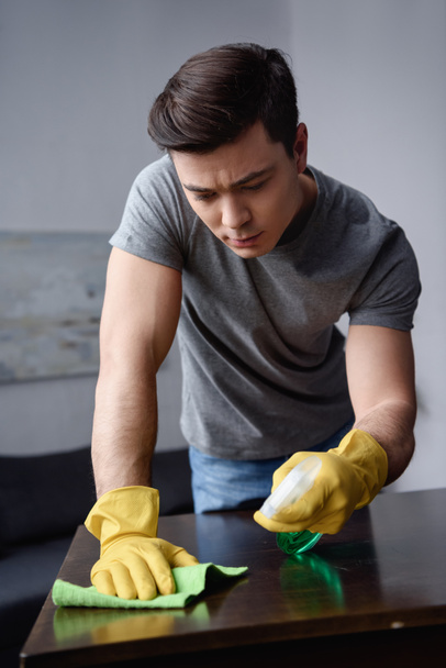 handsome man cleaning table in living room with spray bottle and rag - Photo, image