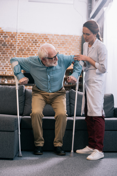 Doctor helping senior patient with crutches - Zdjęcie, obraz