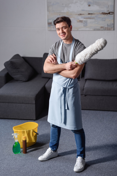uomo bello sorridente in piedi e tenendo pennello per la pulizia della polvere in soggiorno
 - Foto, immagini
