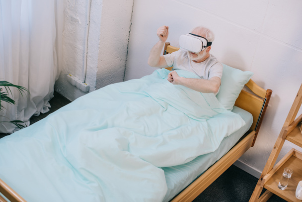 Vanhempi mies potilas kliinisessä sängyssä käyttäen vr-kuulokkeita
 - Valokuva, kuva