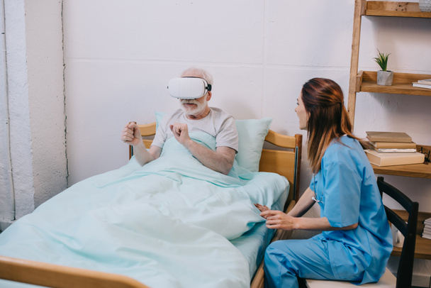 Enfermera sentada por un anciano usando anteojos vr
 - Foto, Imagen