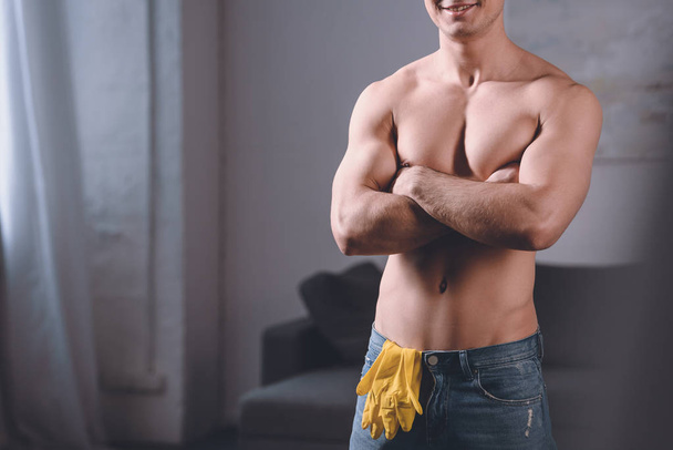 cropped image of seductive shirtless man standing with crossed arms, rubber gloves in jeans - Photo, image