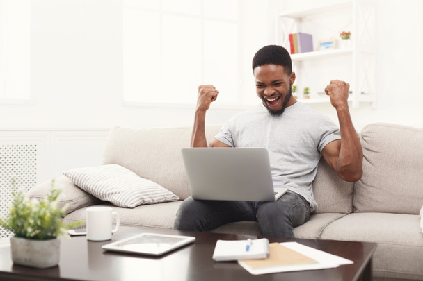 Jeune homme noir avec les bras levés, avec ordinateur portable célébrant le succès
 - Photo, image