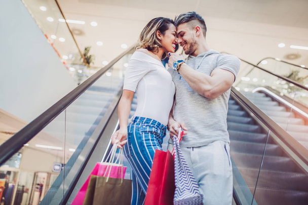  幸せな若いカップルがモールのエレベーターを使用して買い物袋  - 写真・画像