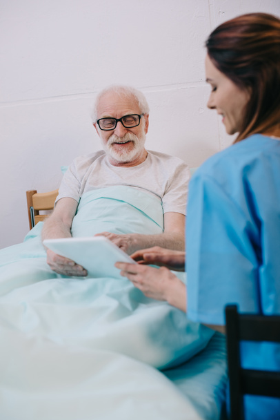Старший пациент в постели и медсестра с помощью таблетки
 - Фото, изображение