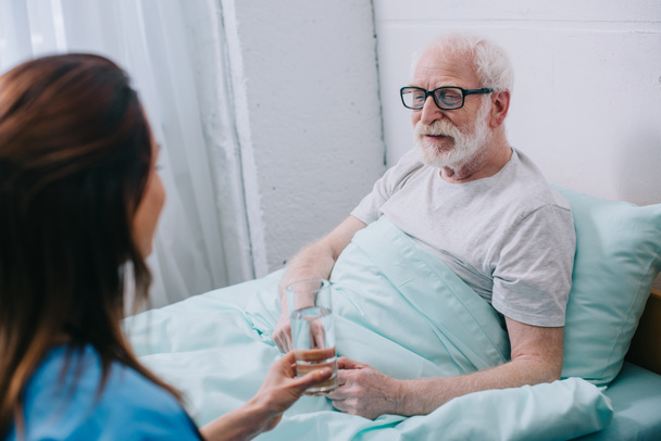 Nurse giving old man in bed a glass of water - Photo, Image