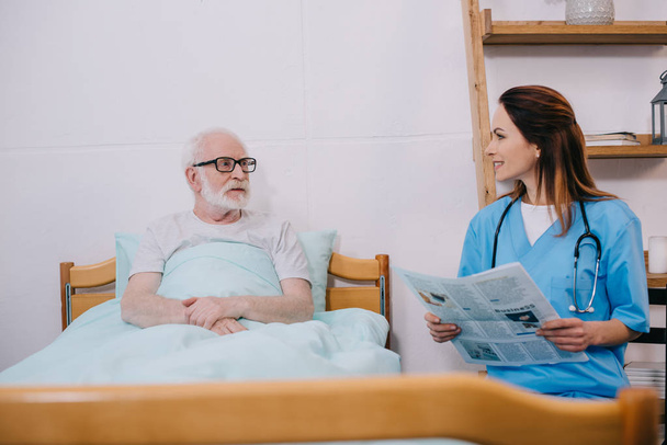Nurse reading newspaper to senior patient  - Photo, Image