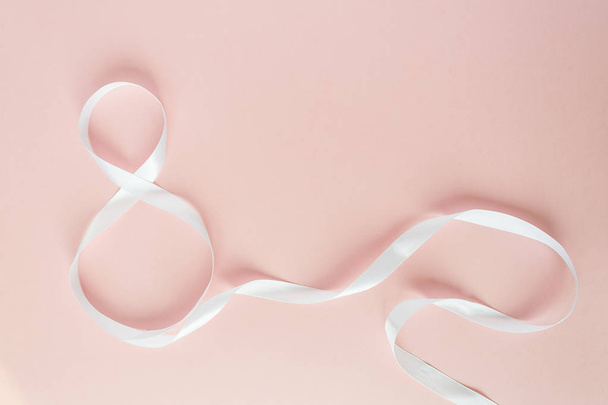 White gift celebration ribbon in 8 digit shape over pink background - Foto, afbeelding