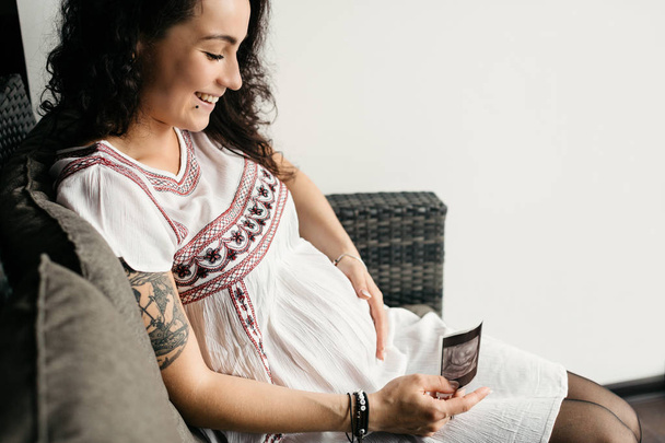 Портрет счастливой беременной женщины, трогающей живот и смотрящей на скан своего ребенка
. - Фото, изображение