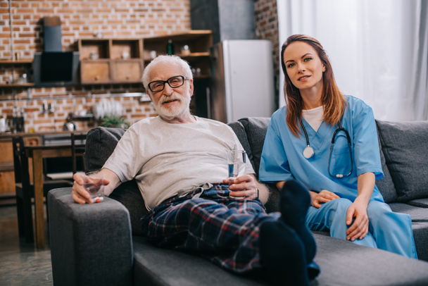 Senior patient with pills and nurse sitting on sofa - Fotografie, Obrázek
