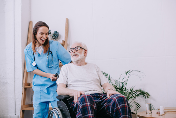 Infirmière rieuse et patiente âgée en fauteuil roulant
 - Photo, image