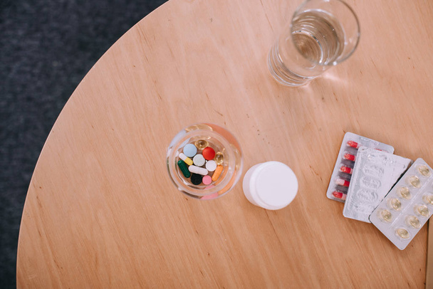 Diferentes píldoras y cápsulas de colores con vaso de agua en la mesa
 - Foto, Imagen