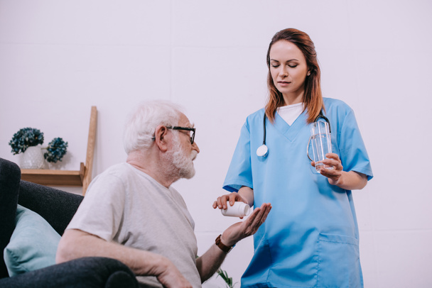 Pielęgniarka stojący przez starszy człowiek biorąc leki - Zdjęcie, obraz