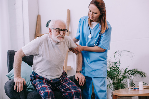 Krankenschwester hilft altem Mann, vom Stuhl aufzustehen - Foto, Bild