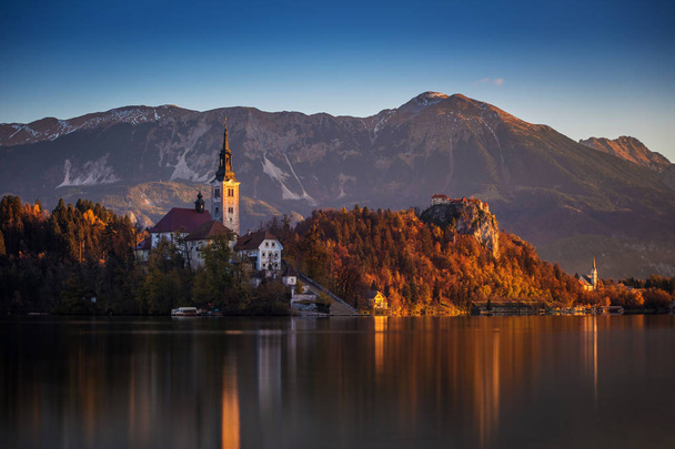 Μπλεντ, Σλοβενία - όμορφο φθινόπωρο Ανατολή του ηλίου σε Λίμνη Μπλεντ με την περίφημη εκκλησία προσκυνήματος της Κοιμήσεως Θεοτόκου της Μαρίας με το κάστρο του Bled και τις Ιουλιανές Άλπεις στο παρασκήνιο - Φωτογραφία, εικόνα
