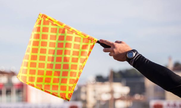 Soccer referee assistant raises the flag with his hand. Blur blue sky and buildings background, close up view. - Photo, Image