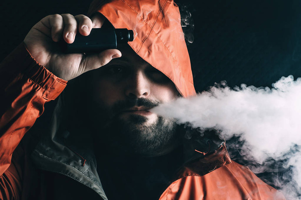 Homem fumante vaping e-cigarro com e-líquido de vape dispositivo RDA, respira vapor e olha para a câmera. Conceito de violação
 - Foto, Imagem