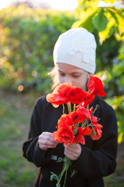 cute little girl in a coat and hat holding a bouquet of poppy flowers in the spring - Foto, Imagem