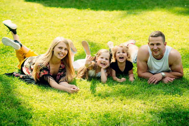 Vacation, leisure, activity, lifestyle concept. Mothers and fathers day. Children and parents lie on green grass. Happy childhood, family, love. Girls, woman and man smile on summer landscape. - Photo, image