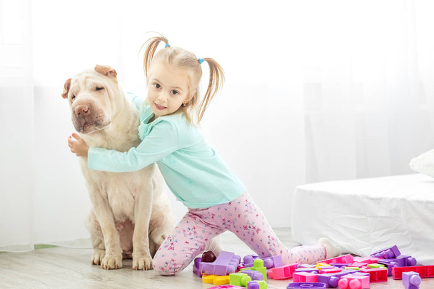 Маленький ребенок обнимает собаку в комнате. Концепция образа жизниc
 - Фото, изображение