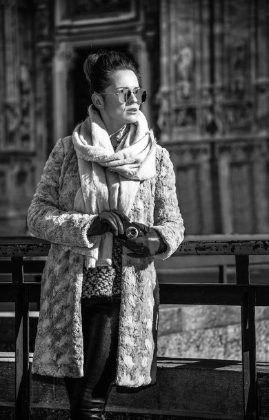elegant woman in fur coat and sunglasses in Milan, Italy looking into the distance while holding digital photo camera - Photo, Image