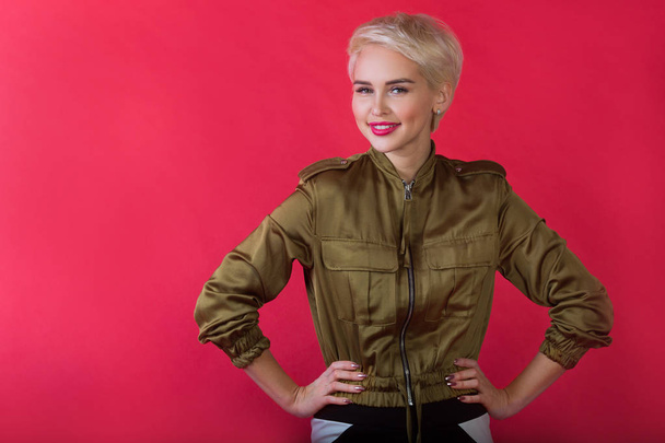 beautiful young girl with a smile and with a short hairdo in a jacket on a red background - Foto, Bild