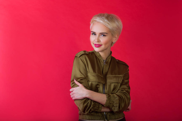 beautiful young girl with a smile and with a short hairdo in a jacket on a red background - Photo, image