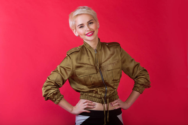 beautiful young girl with a smile and with a short hairdo in a jacket on a red background - Photo, image