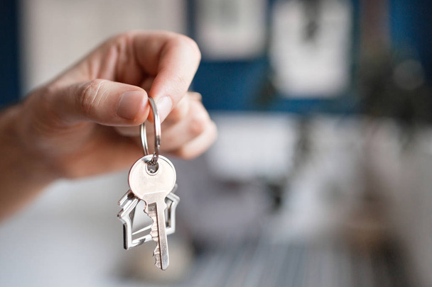 Концепция ипотеки. Мужчины держат ключ с брелоком в форме дома. Современный светлый вестибюль. Недвижимость, переезд или аренда недвижимости
. - Фото, изображение