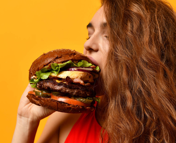 Woman eat burger sandwich with hungry mouth on yellow background - Фото, изображение