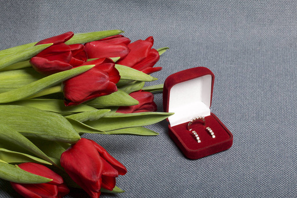 Gifts for loved ones. A bouquet of red tulips. Nearby is a red velvet box with a ring and earrings. - Foto, Imagem