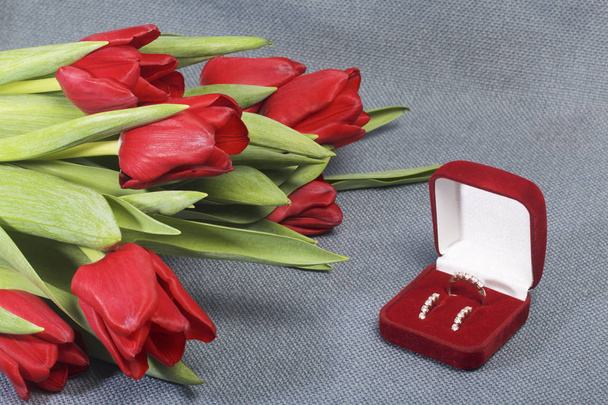 Gifts for loved ones. A bouquet of red tulips. Nearby is a red velvet box with a ring and earrings. - Photo, image