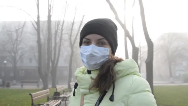 La segunda ola de coronavirus covid-19. Mujer joven de pie en la calle de la ciudad en máscara médica protectora en otoño - Imágenes, Vídeo