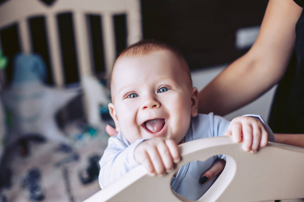 A newborn is smiling happily. Mom supports the baby in a cot - Photo, Image