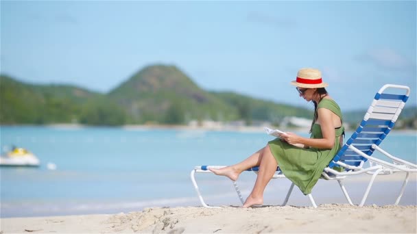 Mujer joven leyendo libro sobre tumbonas en la playa tropical blanca
 - Imágenes, Vídeo
