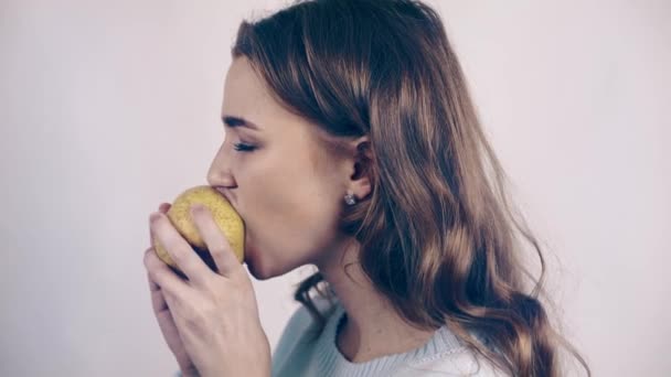 Pretty woman biting a pear and looking at camera - Кадри, відео