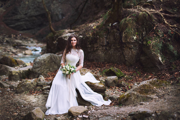The bride sits on stones high in the mountains by the river - Foto, afbeelding