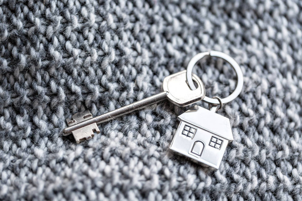 Ключ от дома и брелок в виде домов лежат на трикотажной шерстяной ткани. Концепция недвижимости, ипотеки, переезда или аренды недвижимости
. - Фото, изображение